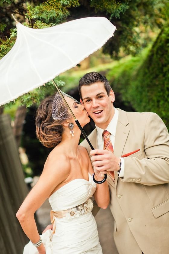 Bride kissing groom under an umbrella