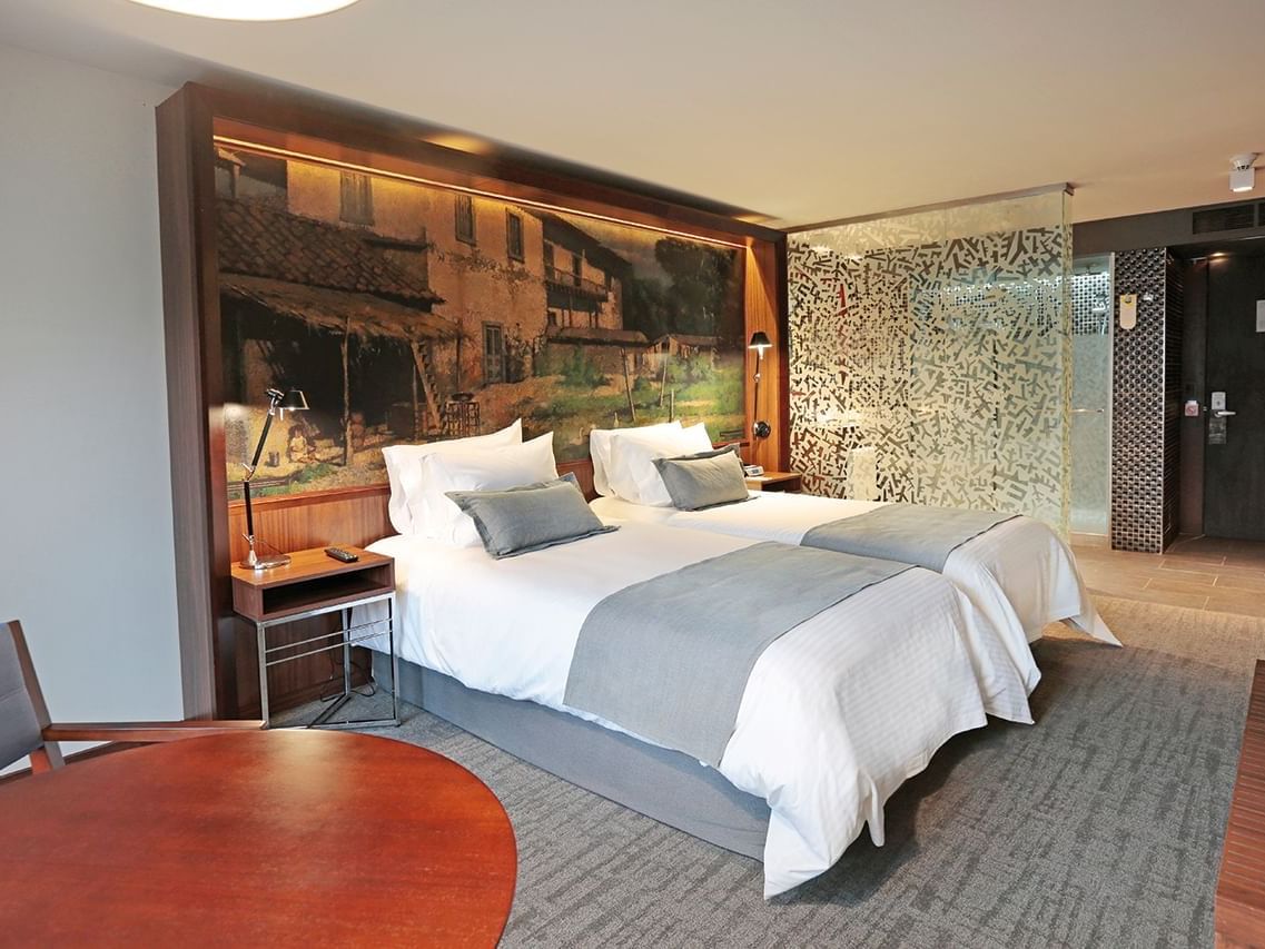 Superior Twin Double hotel room with two beds, large painting, glass partition, table, and chair.