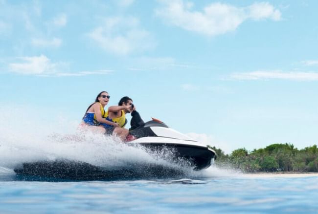 Two people parasailing with a colorful parachute high above a boat under a cloudy sky at Shangri-La Resort and Golf Club
