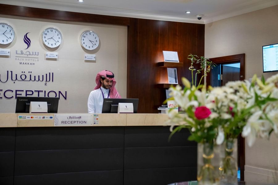Hotel receptionist in traditional attire working at the front desk counter at Saja by Warwick Makkah