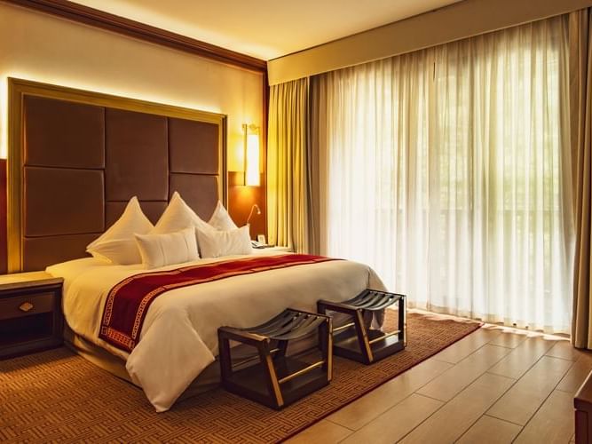 Spacious deluxe room with king bed, wooden accents, floor-to-ceiling curtains, and warm lighting at Sumaq Machu Picchu Hotel