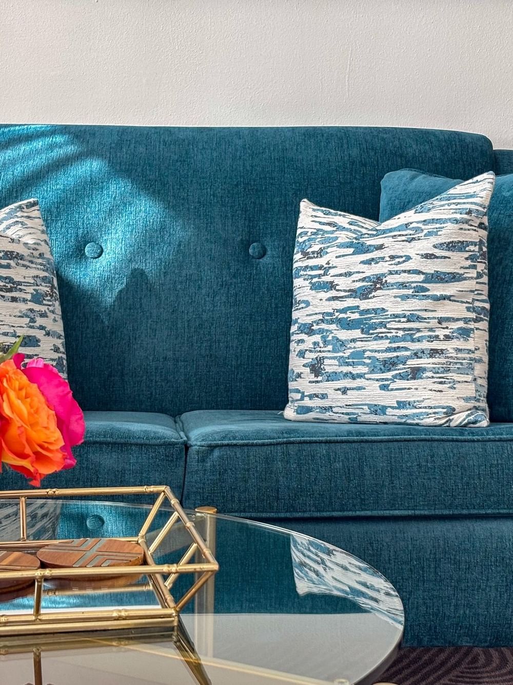 Blue couch with floral pillows and flower arrangement on a glass table at Warwick Melrose Dallas.