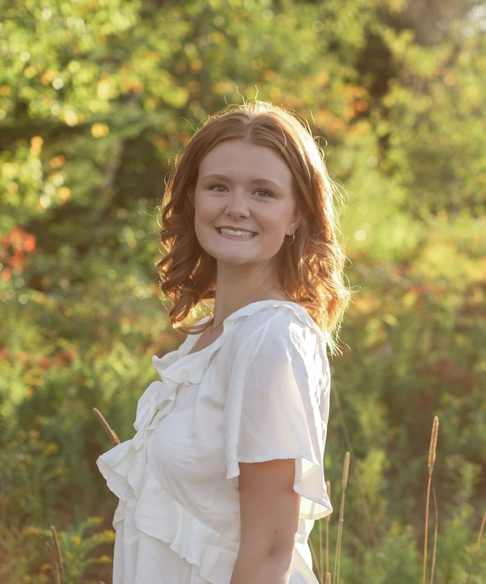 Portrait of smiling Abi in a ruffled white top standing amid tall grass outdoors at Rodd Brudenell River Resort