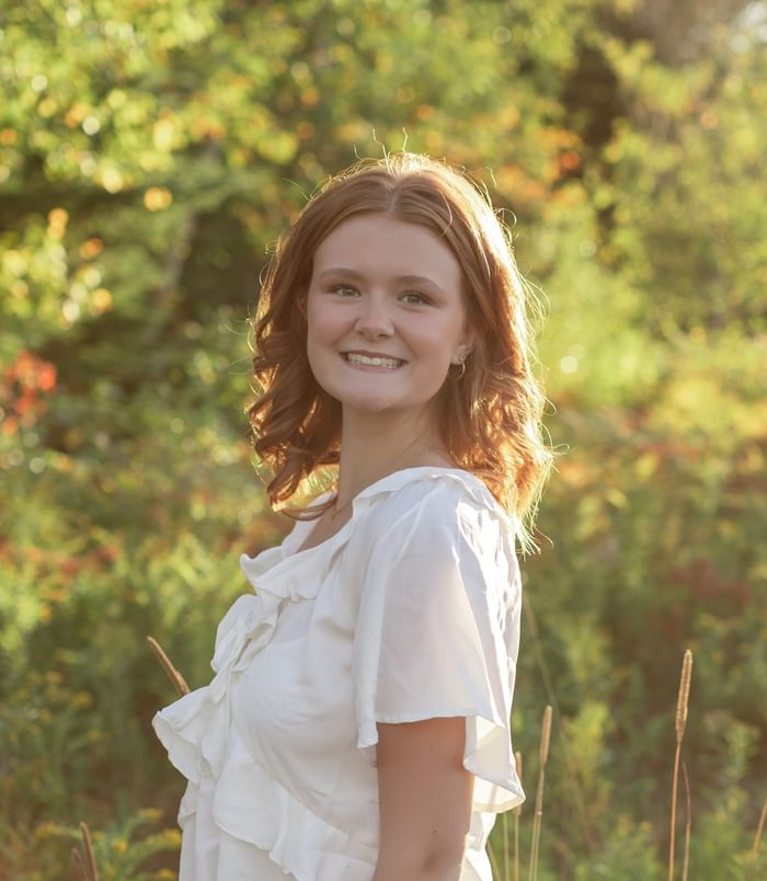 Portrait of smiling Abi in a ruffled white top standing amid tall grass outdoors at Rodd Brudenell River Resort