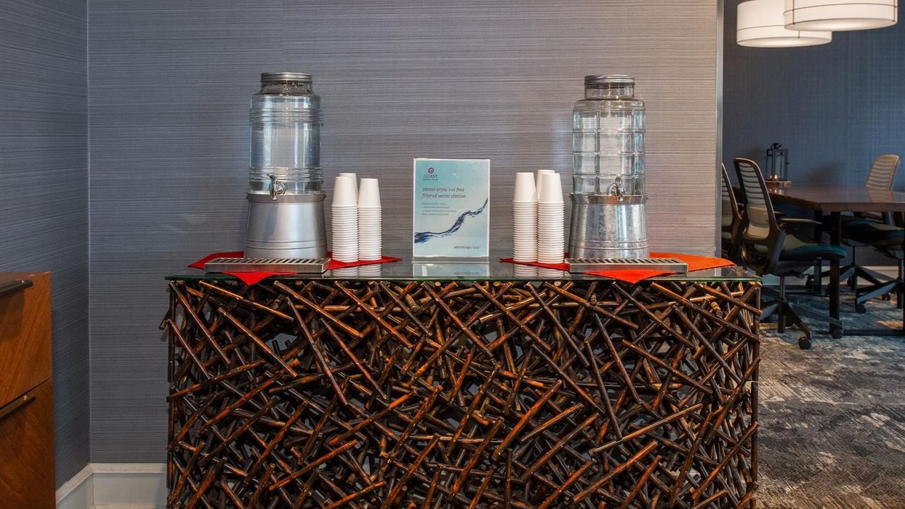 Water dispensers and cups on a unique wooden counter at Coast Bastion Hotel.