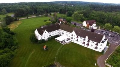 High-angle aerial view of the La Tourelle Hotel and Spa with a parking lot surrounded by vast forest