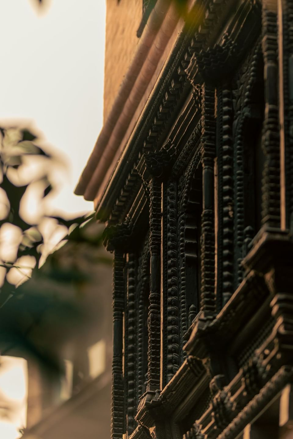 Wooden carvings adorn the corner of a traditional building, illuminated by soft sunset light at Dwarika's Hotel Kathmandu