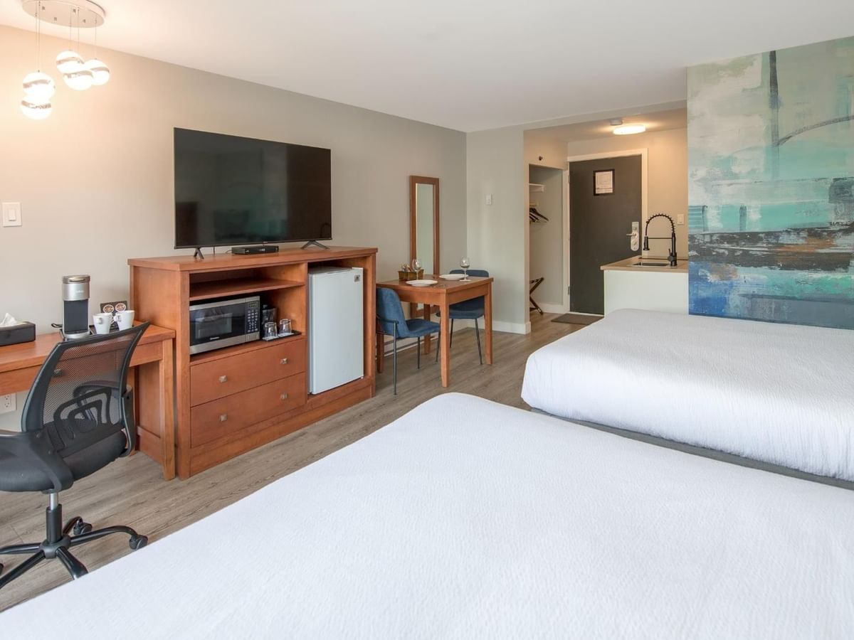 Hotel room with two queen beds, a desk, chair, TV, mini-fridge, microwave and a small kitchenette.