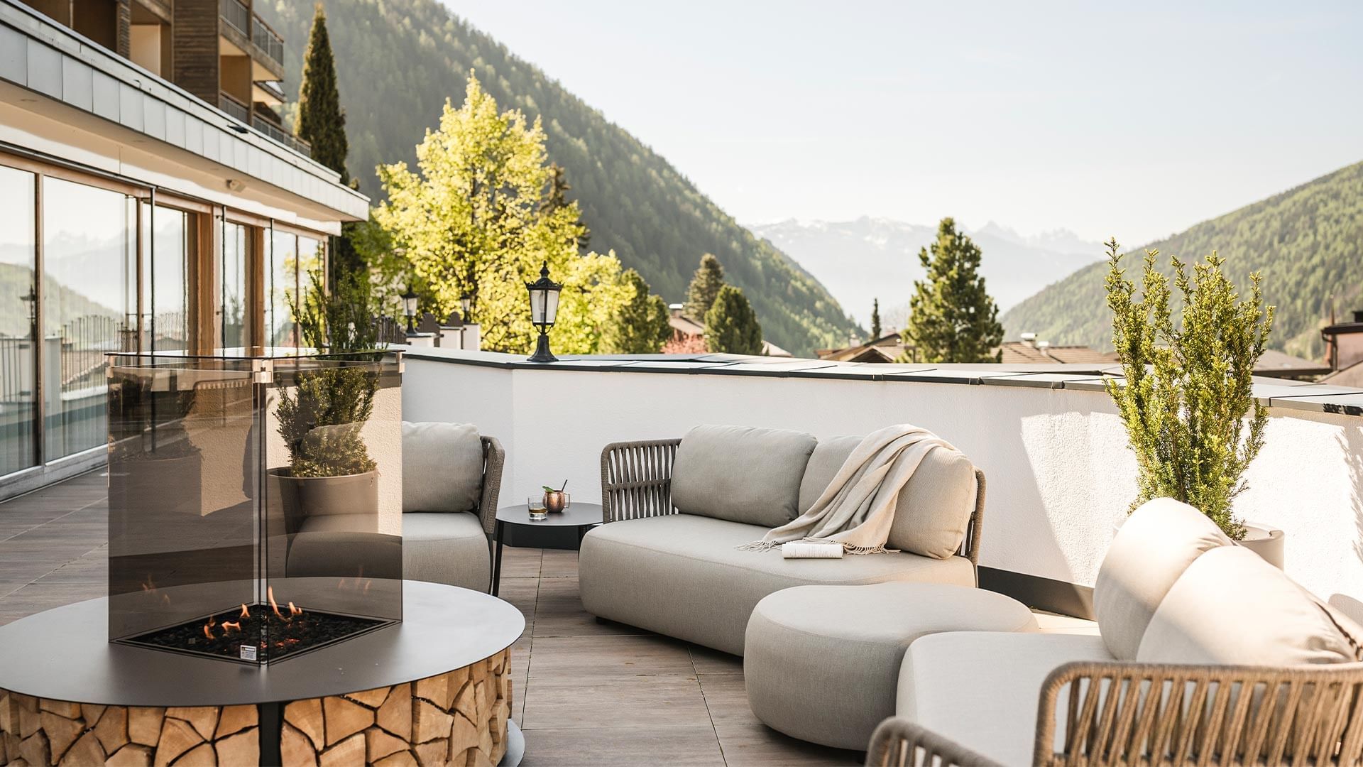Terrasse mit Sitzmöbeln, Feuerstelle und Blick auf Berge und Wälder.
