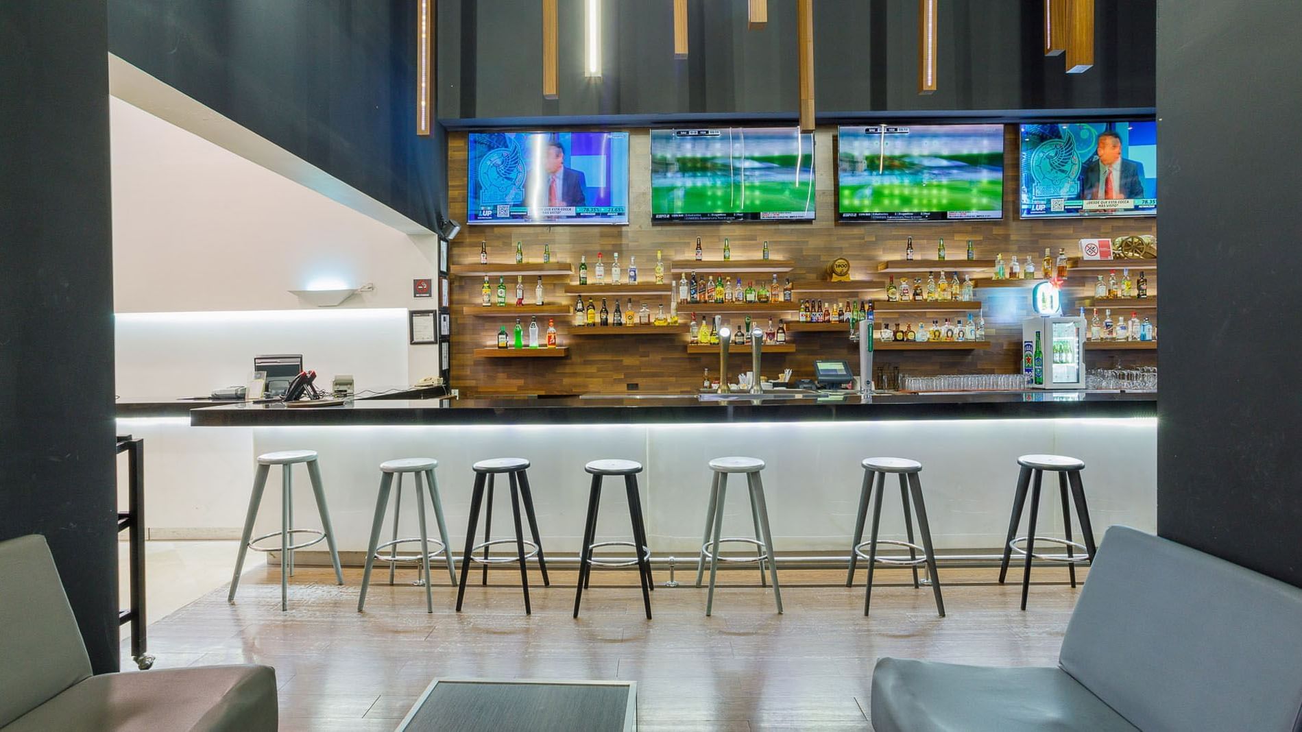 Stock Bar with white stools and wall-mounted sports televisions at Real Inn Tijuana