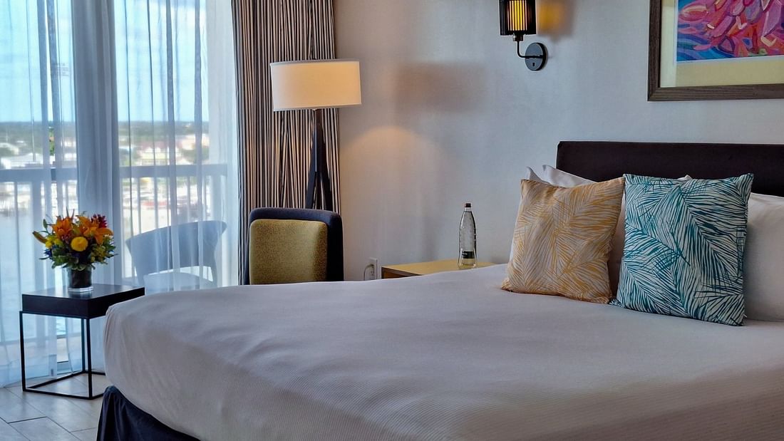King bed with patterned pillows by an armchair and floor lamp in Harbour Deluxe Balcony at Warwick Paradise Island Bahamas
