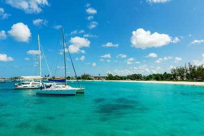 Two white catamarans anchored in crystal turquoise Caribbean waters by a white sandy beach near The Abidah Hotel