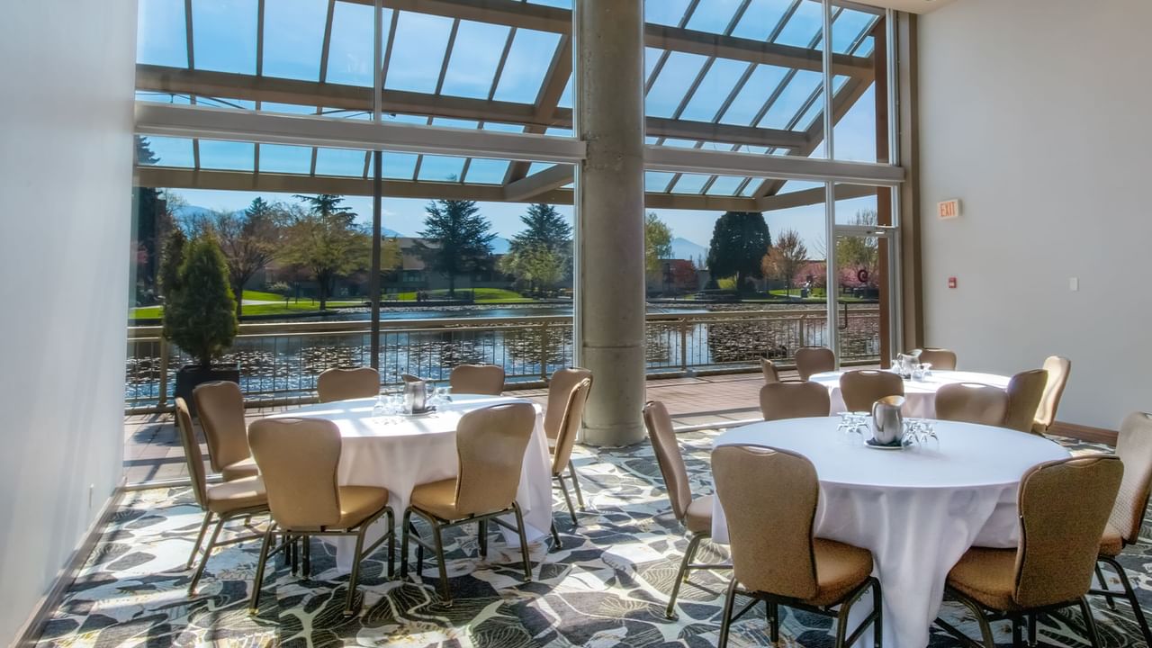 Meeting room with large windows, tables with white tablecloths, and chairs.