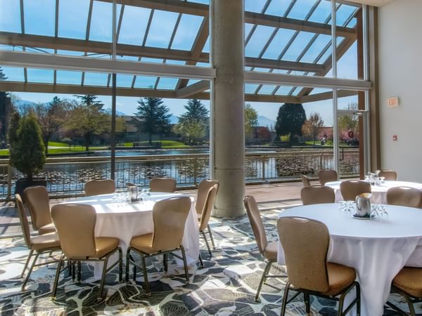 A meeting room with large windows and round tables with chairs, overlooking a pond.