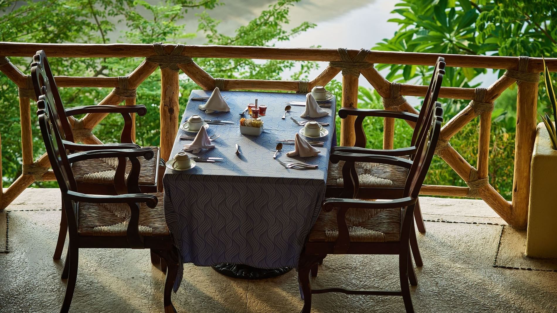 Intimate dinner table in Tierra Mia set with blue linens on a terrace near lush green trees at Quinta Real Acapulco
