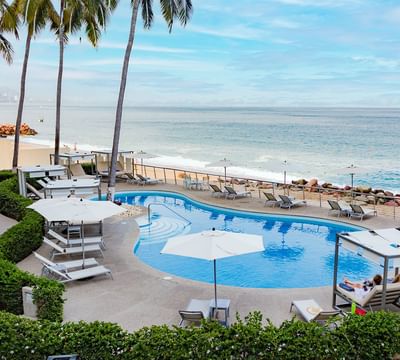 Piscina con tumbonas, sombrillas y una palapa con vistas a la playa de Puerto Vallarta en el Sunset Plaza Beach Resort