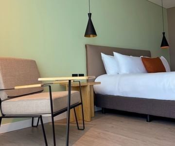 Guest room with a gray armchair and wooden table beside a white bed at Unika Hotels, a featured hotel in Bogota, Colombia