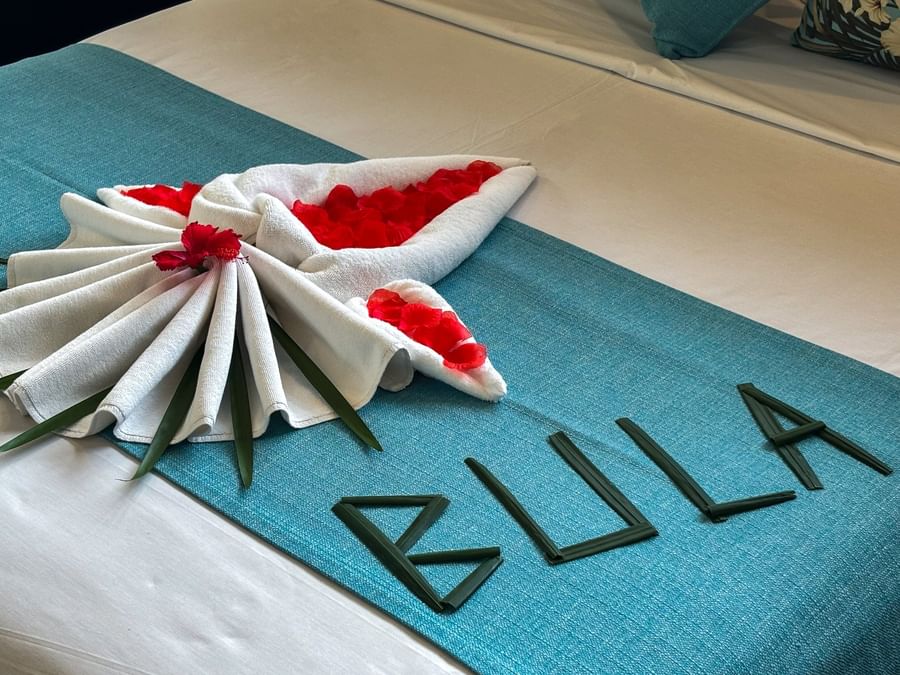 Teal bed runner featuring leaf lettering and a white towel fan with red petals in Family Villa at TokaToka Resort Nadi Fiji