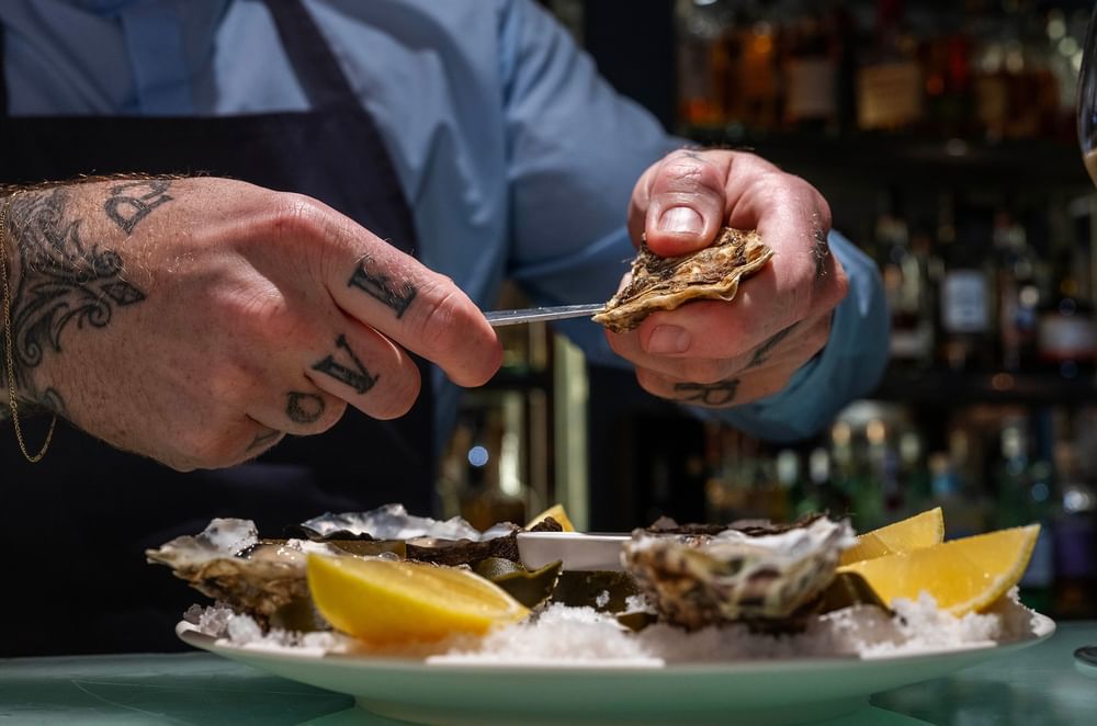Chef shucking fresh oysters by a plate of lemon wedges on a counter at The Capital Hotel, Apartments and Townhouse