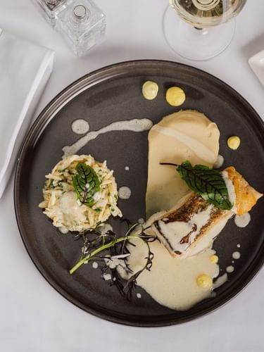  Gourmet plated fish on a dark plate, with a glass of wine and a bread roll, in Sunday Brunch at Warwick Geneva