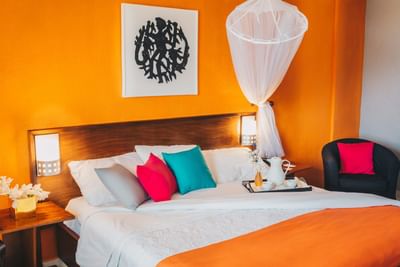 Bed with a coffee tray and colorful pillows by a black armchair under a canopy net in Superior Room at Hotel Montana Haiti