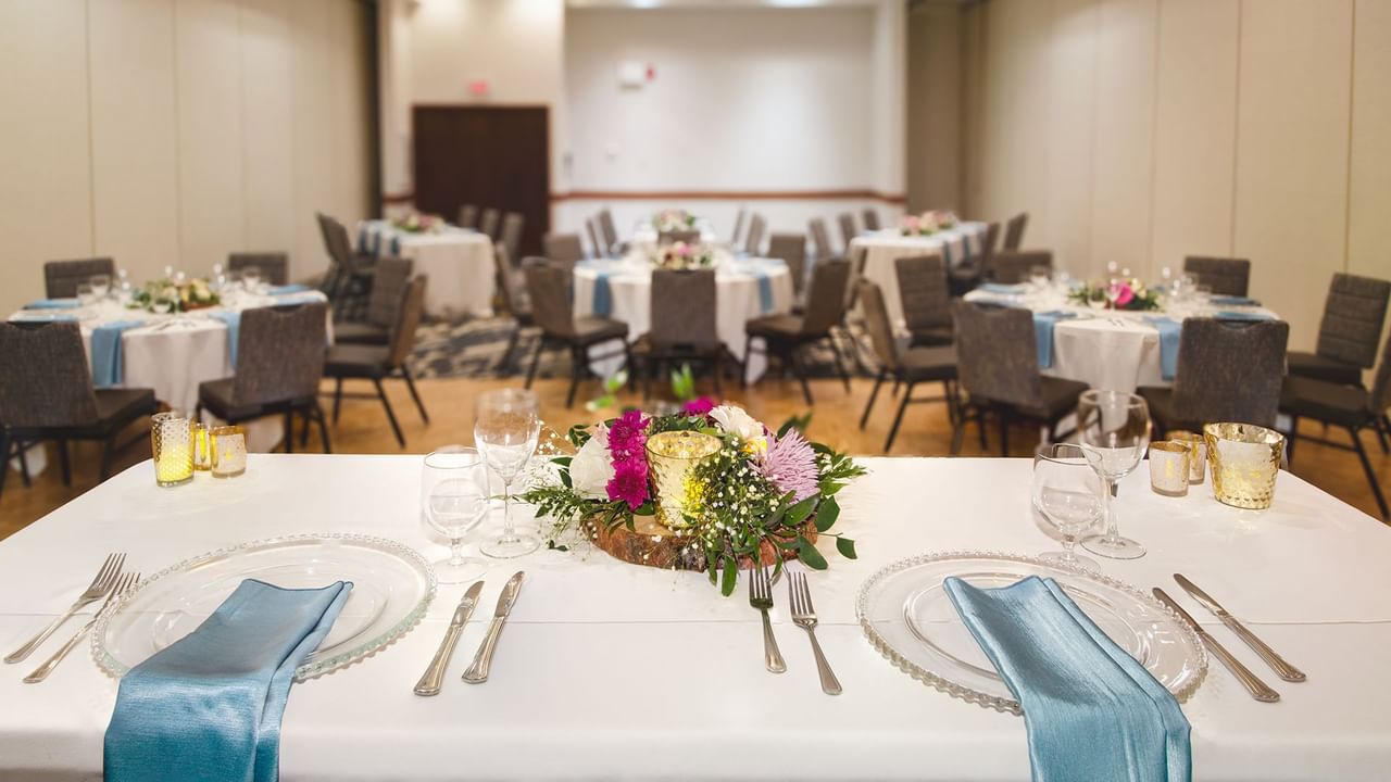 A banquet hall with multiple tables set, each adorned with floral arrangements.