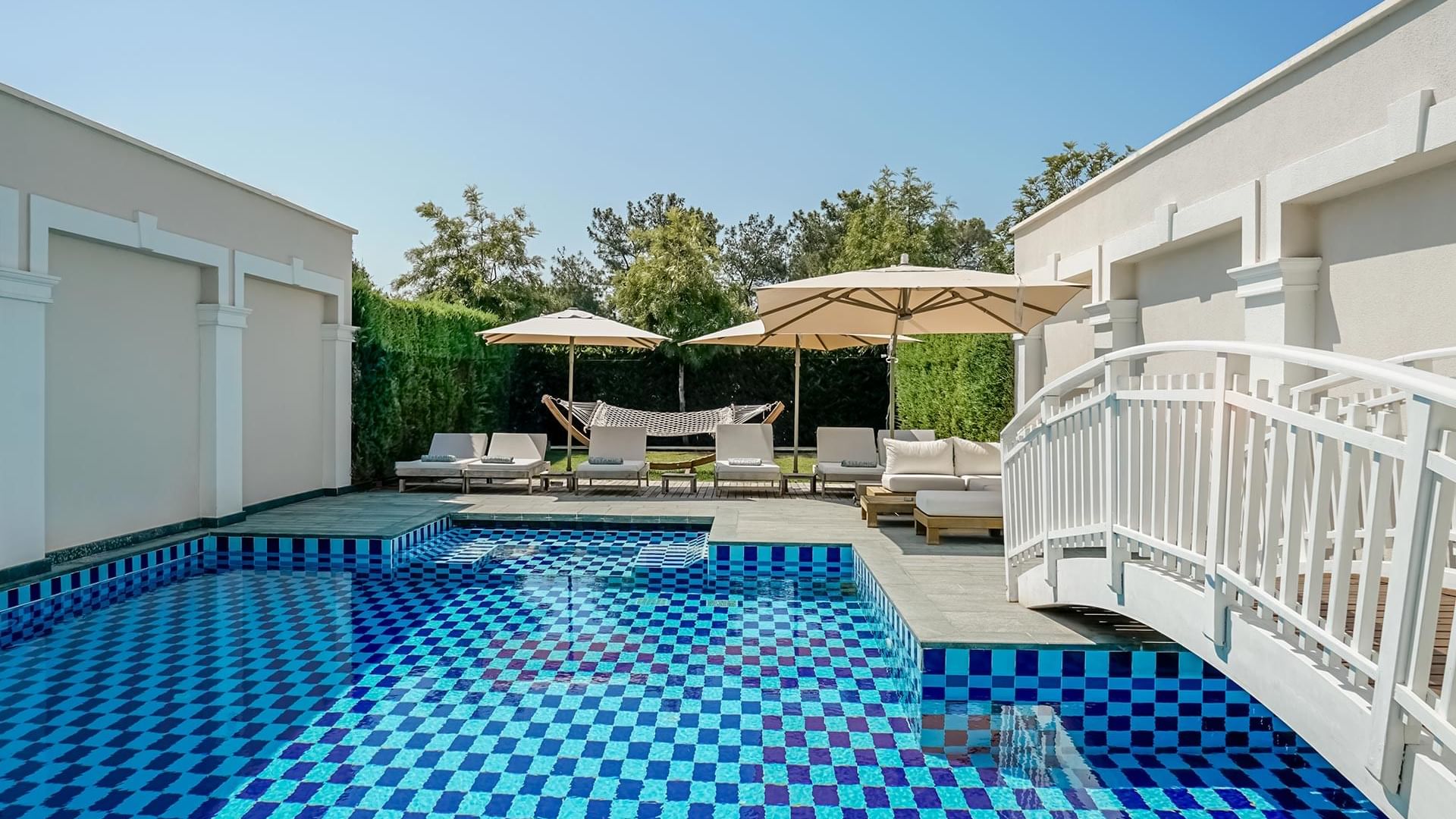 Titanic Deluxe Golf Belek'teki Design Pool Villa'da havuz terasında güneşlenme şezlongları ve veranda şemsiyeleri.