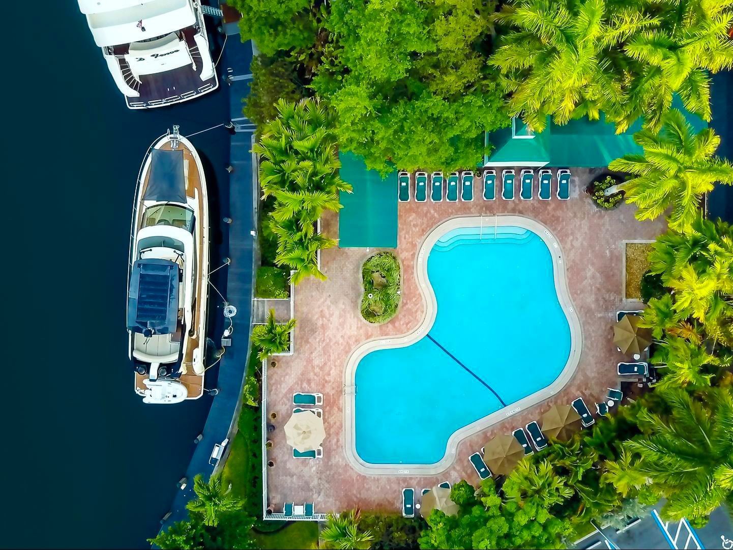 Aerial view of a pool surrounded by palm trees, lounge chairs, and a luxury yacht at Riverside Hotel Fort Lauderdale