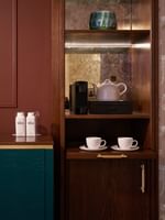 Wooden cabinet with coffee machine, teapot, and water bottles in Deluxe King at The Capital Hotel, Apartments & Townhouse