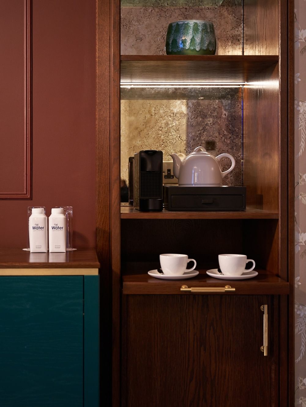 Wooden cabinet with coffee machine, teapot, and water bottles at The Capital Hotel, Apartments & Townhouse