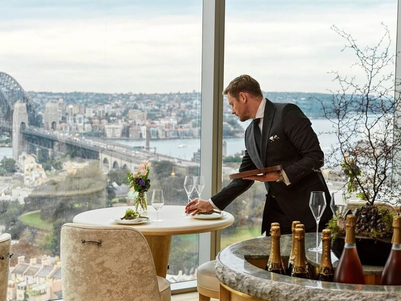 Waiter setting a table in a restaurant with a view of a bridge and cityscape at Crown Hotels