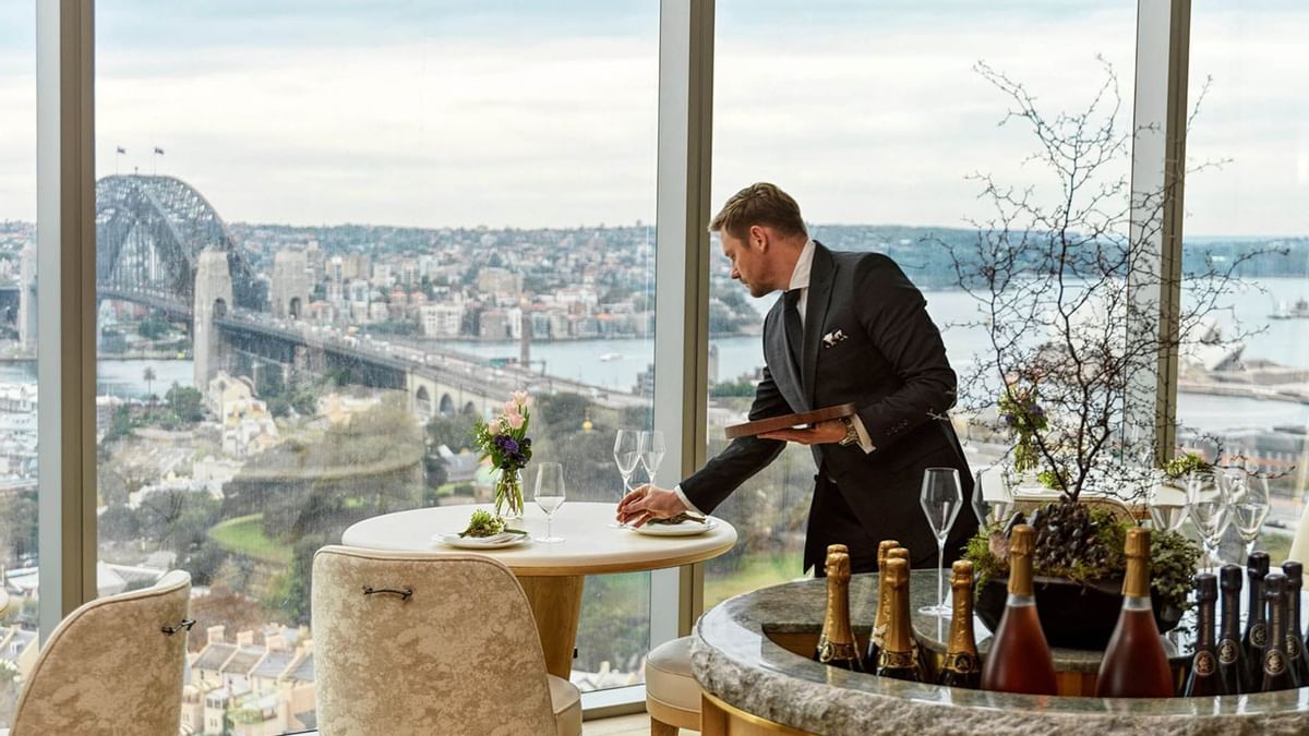 Waiter setting a table in a restaurant with a view of a bridge and cityscape at Crown Hotels