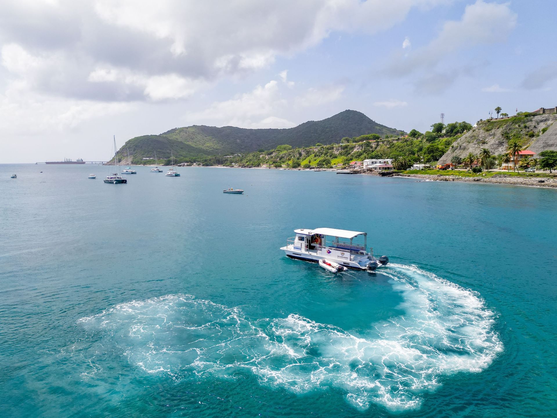 Small boat creating whirlpools in turquoise water by a lush green hillside, and anchored yachts near Golden Rock Resort