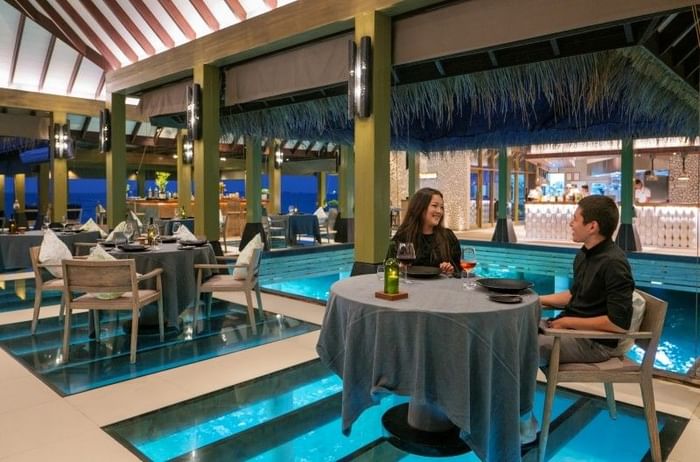 Couple dining at a table in Firedoor fine dining restaurant over glass floor at Grand Park Kodhipparu
