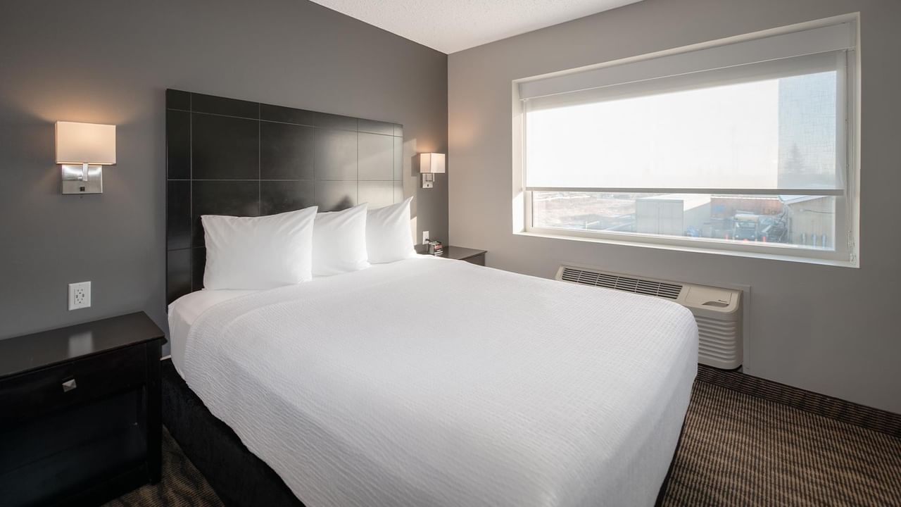 A white bed with pillows in a hotel room with window