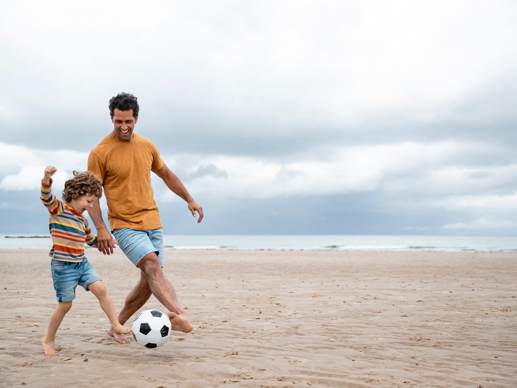 Dad playing soccer with son on the beach by the ocean