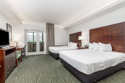 TV and work desk facing the cozy beds in Queen River View Room with carpeted floors at Off Shore Resort