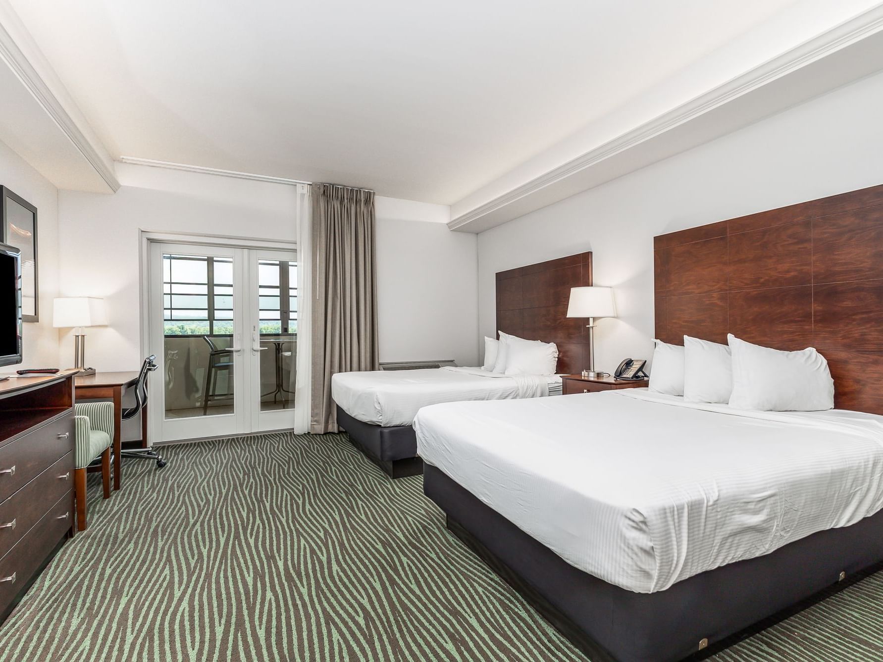 TV and work desk facing the cozy beds in Queen River View Room with carpeted floors at Off Shore Resort