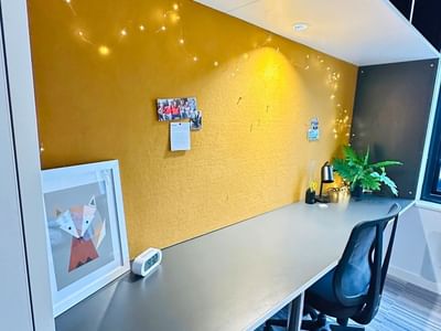 Desk with framed artwork and a plant in a cozy workspace at UniLodge Auckland City.