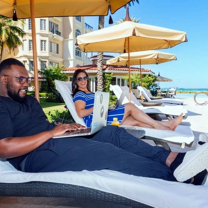 Couple on sunbeds with laptops at The Somerset on Grace Bay