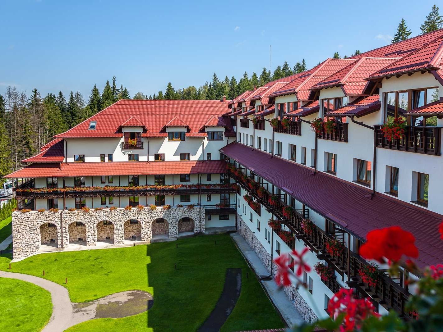 Exterior view of the hotel building of Ana Hotels Sport Poiana Braşov around with trees and grass