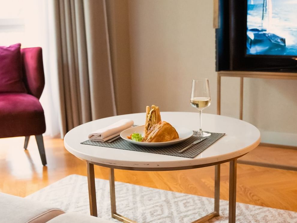Cozy setting with a white round table featuring a sandwich and a glass of wine in a room at Warwick Reine Astrid - Lyon