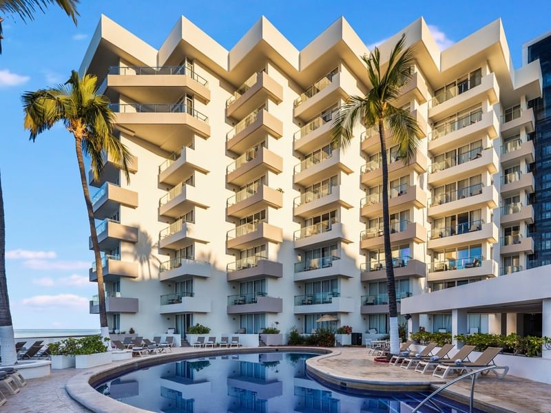 Modern white Sunvivia Mazatlán resort building with tiered balconies overlooking a pool area with tropical palm trees