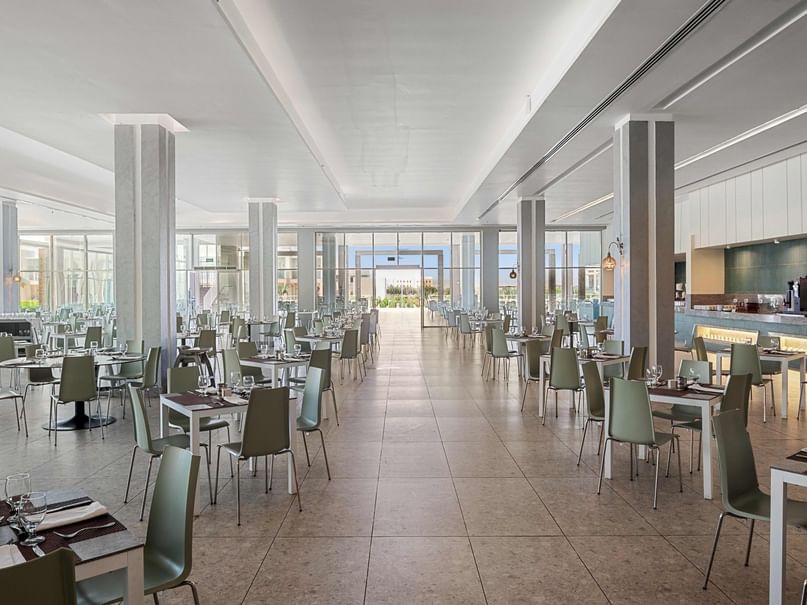 Large dining room with many tables, chairs, and a central walkway leading to a glass-walled entrance.