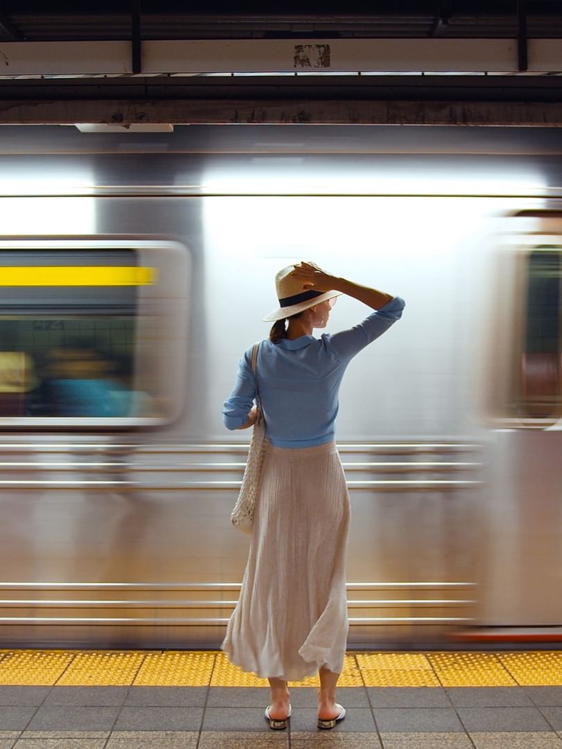 Femme élégante avec chapeau sur un quai de métro alors qu'un train passe en mouvement flou derrière elle