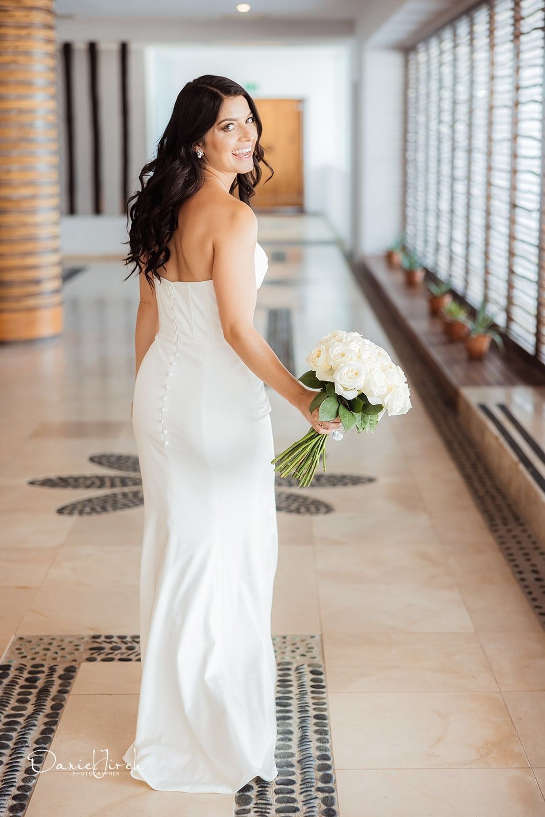 Bride in a strapless white gown holding white roses, smiling back at Marquis Los Cabos Resort