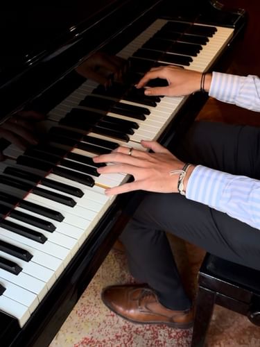 Pianist in a striped shirt playing a black grand piano keyboard from a bench at Lobby Bar, Warwick Brussels Grand-Place