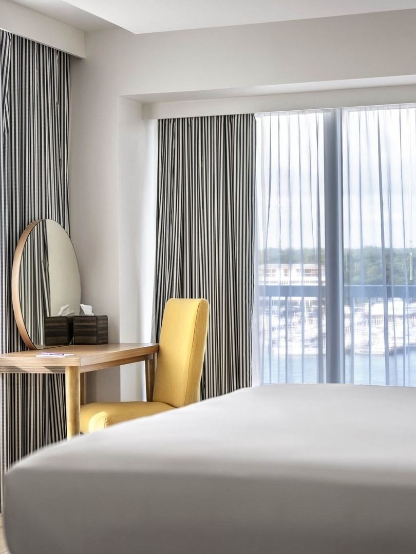 Yellow chair by a wooden desk and a round mirror in One Bedroom Harbourfront Suite at Warwick Paradise Island Bahamas