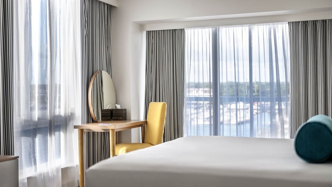 Yellow chair by a wooden desk with a round mirror in One Bedroom Harbourfront Suite at Warwick Paradise Island Bahamas