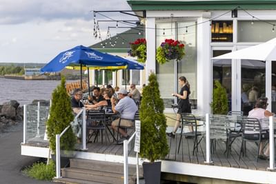 1809 Restaurant & Bar, with patrons eating on an outdoor wooden deck surrounded by small potted trees at Rodd Miramichi River